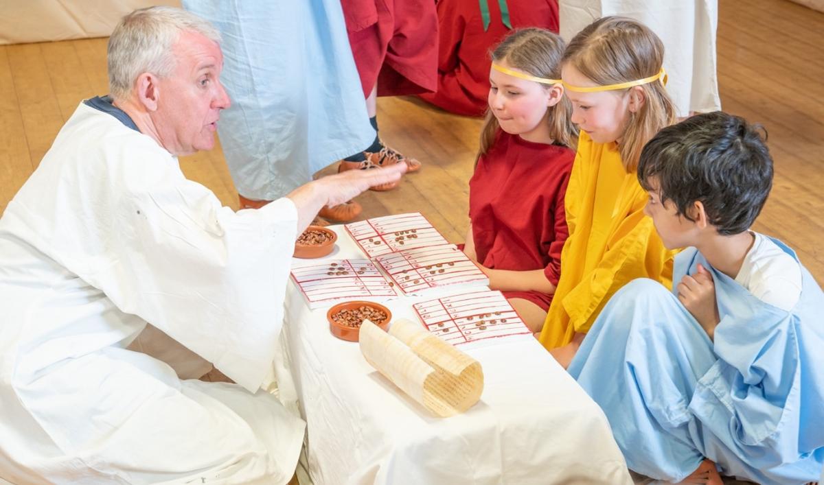 A teacher in a white robe and a group of children sitting at a table.